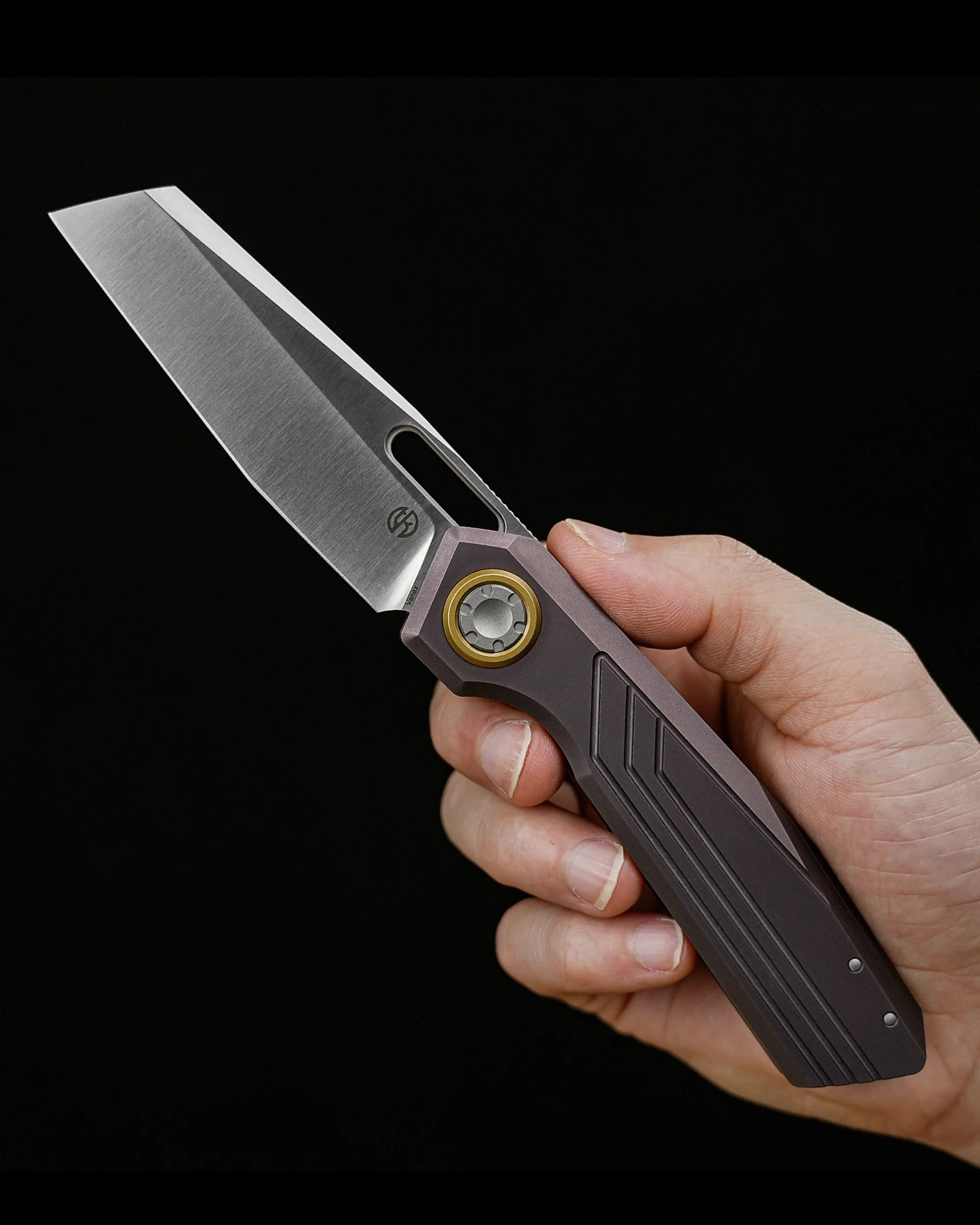 Hand holding a folding knife with a silver tanto blade and a dark gray handle with gold pivot ring.
