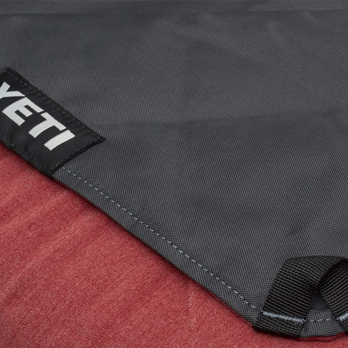 Close-up of a dark gray YETI fabric corner with reinforced stitching and a black loop on a red surface.
