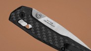 Folding knife with carbon fiber handle and partially visible stainless steel blade engraved with "0117 USA MAGNACUT.
