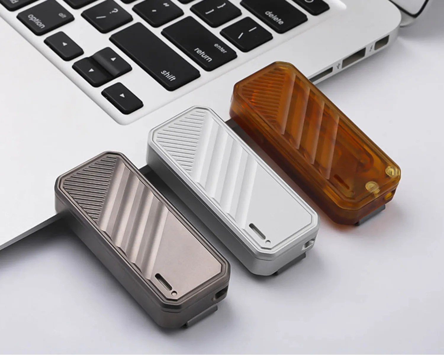 Three rectangular USB flash drives in bronze, silver, and amber colors placed next to a laptop keyboard on a white surface.