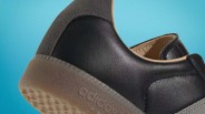 Close-up of black leather Adidas shoe heel with translucent rubber sole and suede heel tab against blue background.