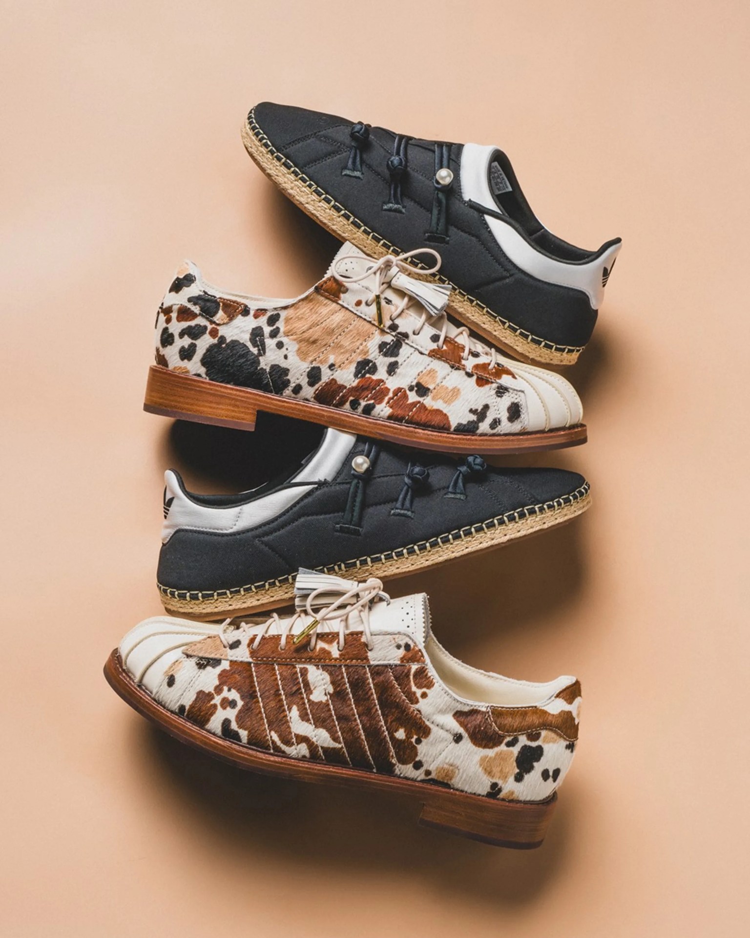 Two pairs of shoes stacked vertically, one pair is black with white accents and jute soles, the other pair has a brown and white cowhide pattern with wooden soles.