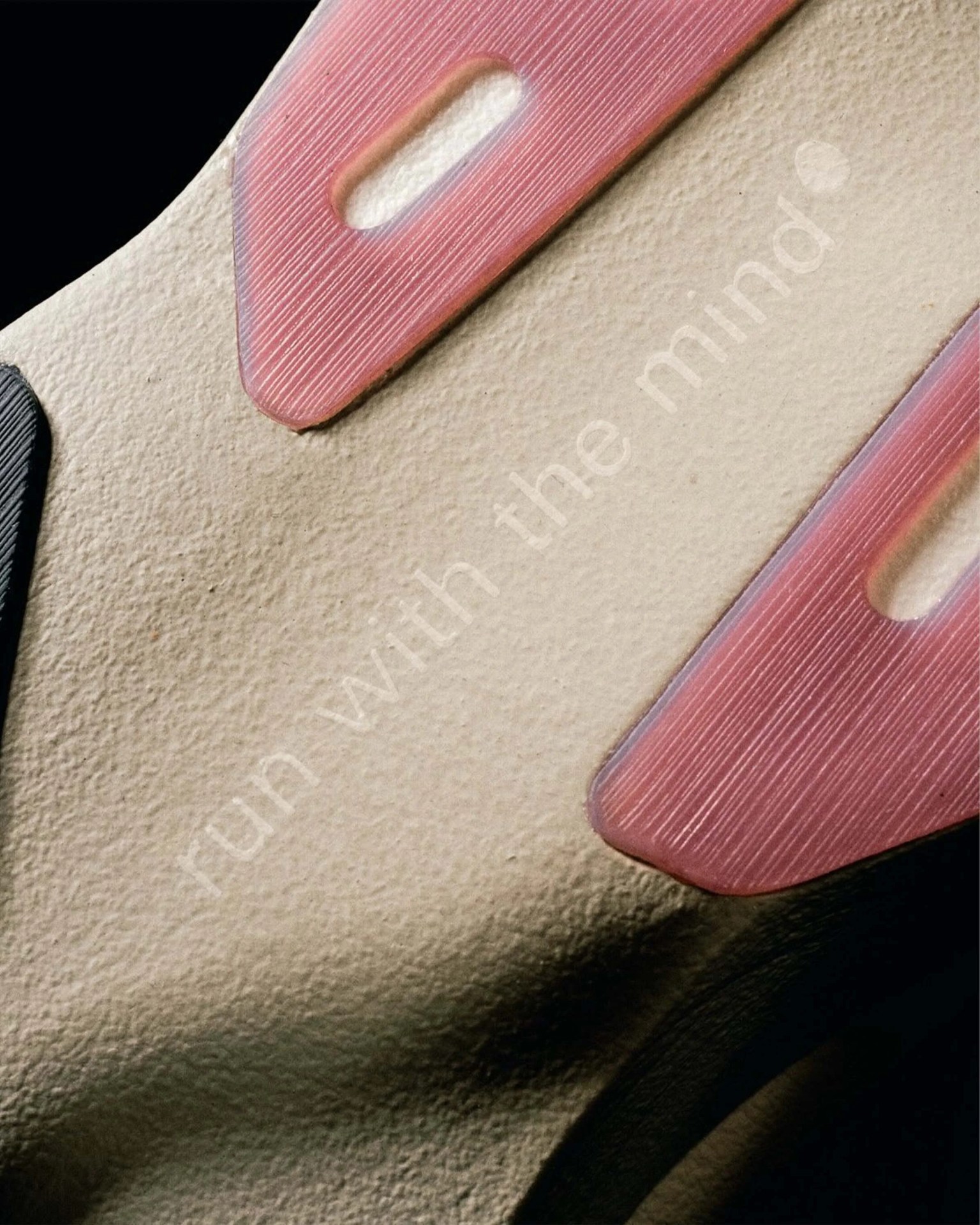 Close-up of a beige textured surface with pink rubber accents and faint white text reading "run with the mind.