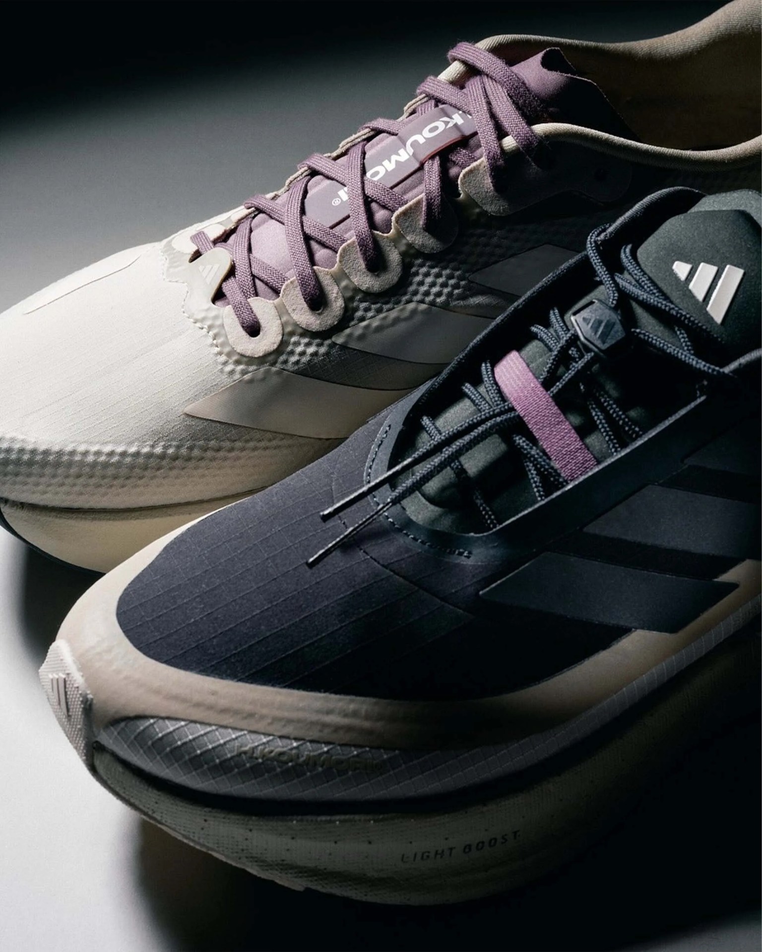 Pair of Adidas running shoes, one in beige with purple laces and one in black with purple lace strap, close-up view.
