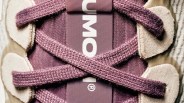 Close-up of purple shoelaces crossed over a purple shoe tongue with beige suede eyelet panels.