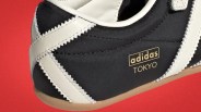 Close-up of black Adidas Tokyo sneaker with white zigzag leather stripes and gum sole on red background.