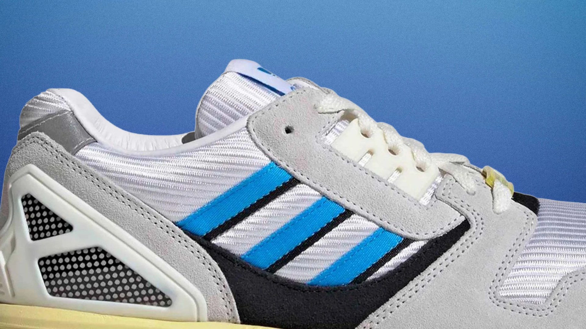 Close-up of a white and gray sneaker with blue stripes and black accents against a blue background.