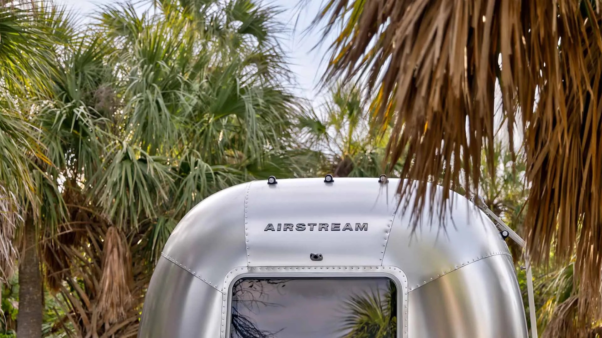Top front of a silver Airstream trailer with palm trees in the background.