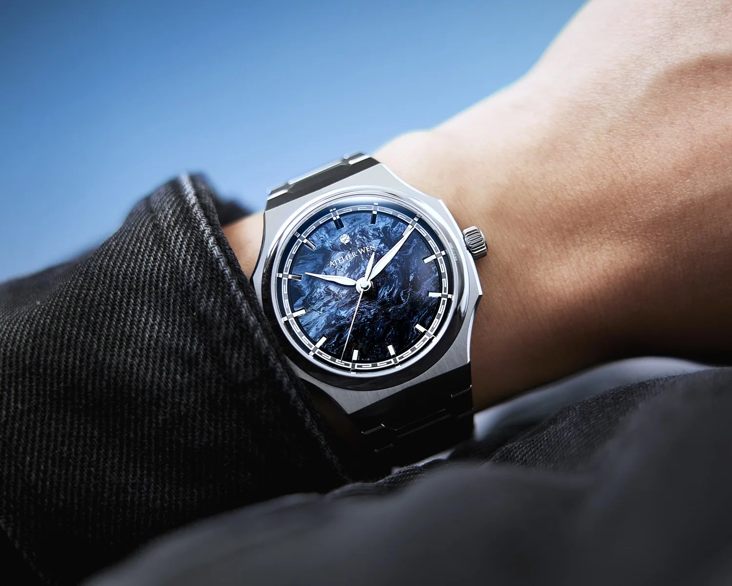 Silver metal wristwatch with a textured dark blue dial and silver hour markers worn on a wrist.