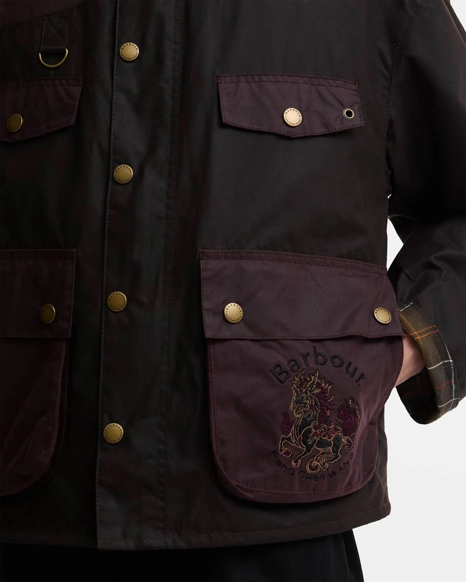 Black and dark purple Barbour jacket with brass snap buttons and embroidered mythical creature on front pocket.