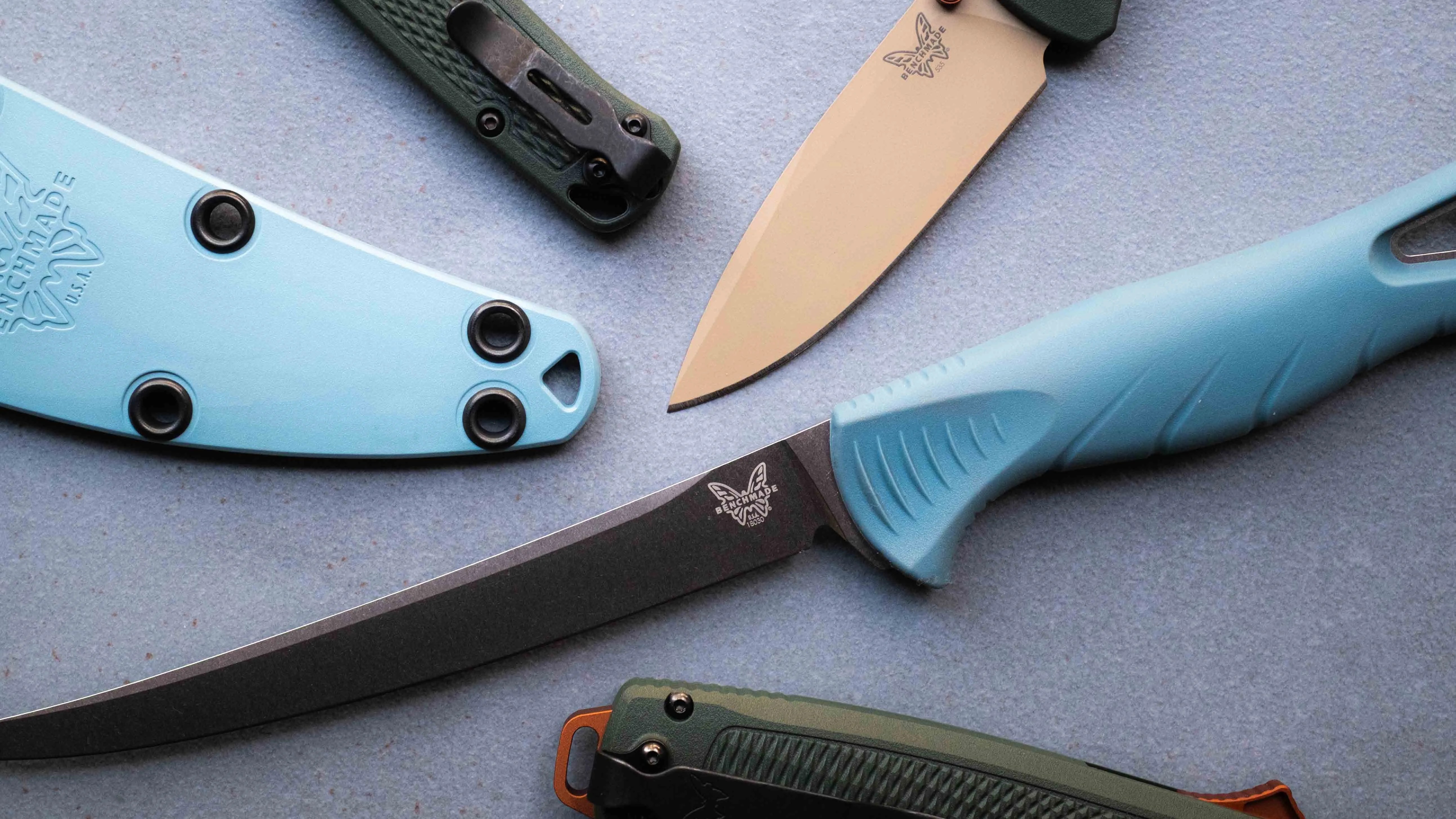 Two Benchmade knives with blue handles and sheaths, and two folding knives with green handles on a gray surface.