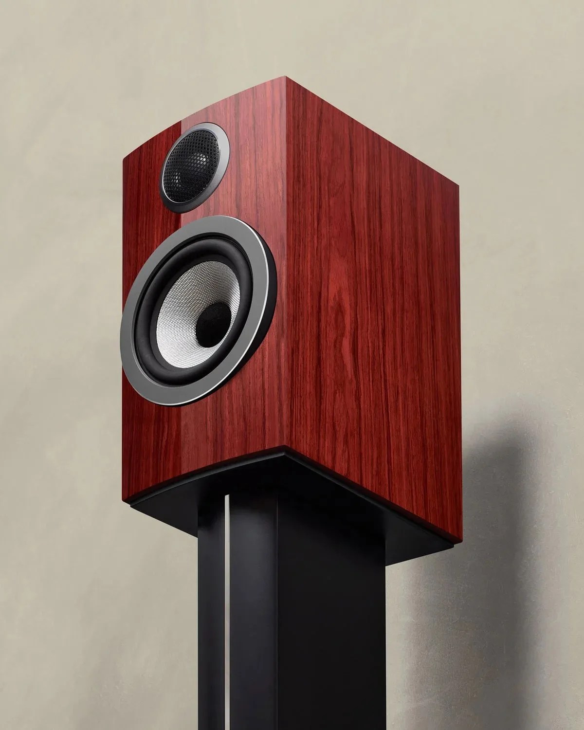 Glossy reddish-brown wooden speaker with silver and black drivers mounted on a black stand against a beige wall.