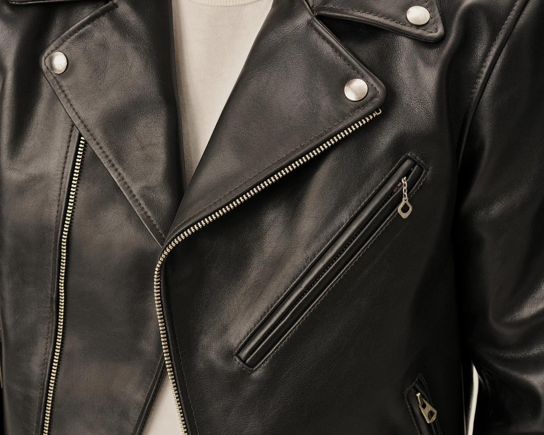 Black leather biker jacket with silver zippers and snap buttons over a beige shirt.