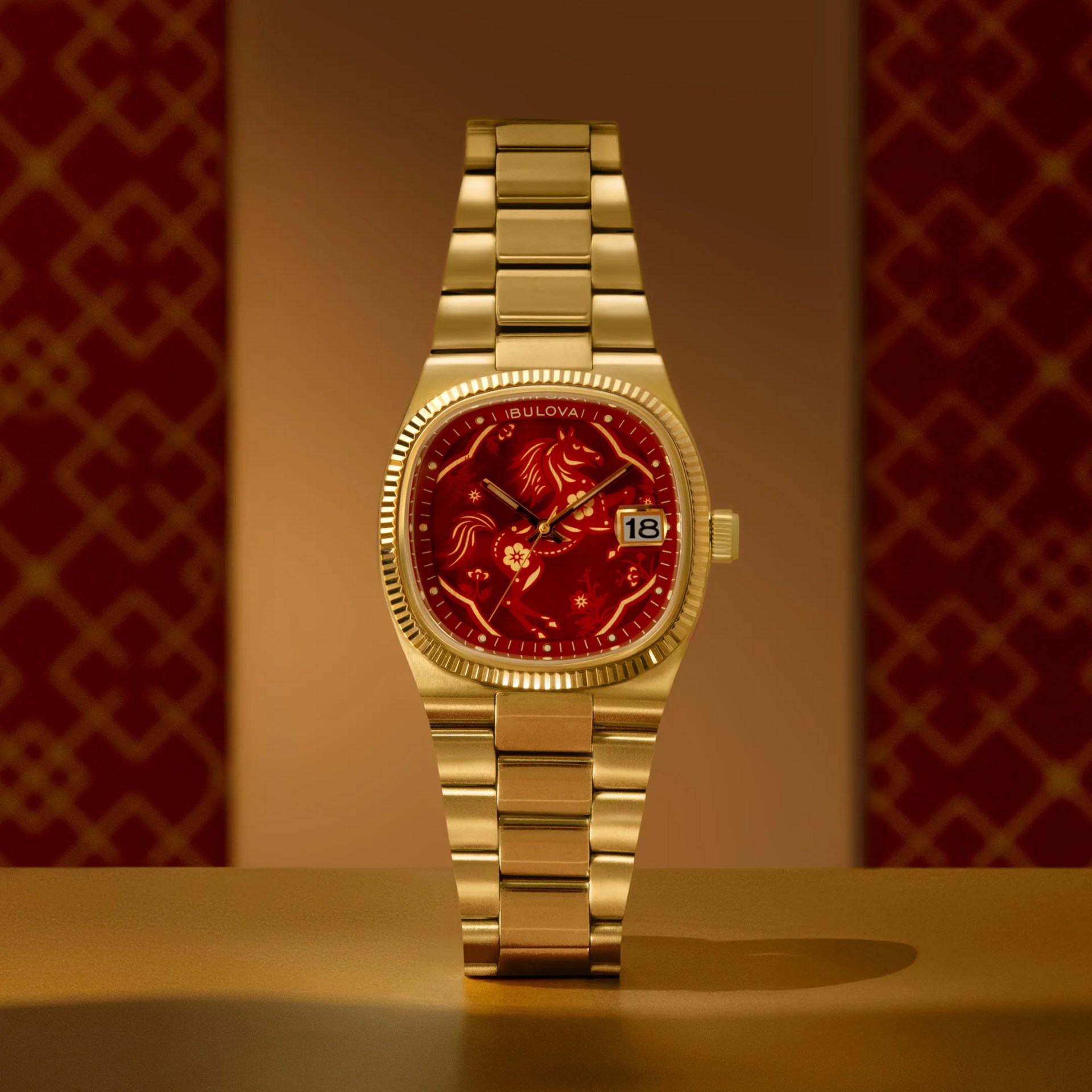 Gold metal wristwatch with a red dial featuring a horse design and a date window showing the number 18.