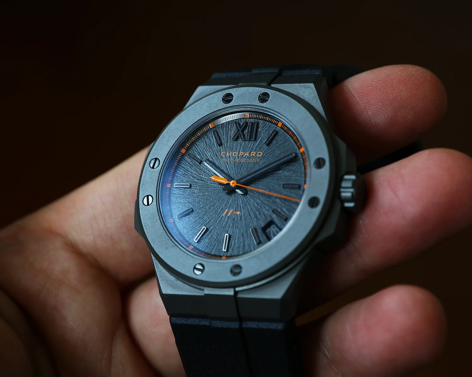 Gray Chopard wristwatch with textured dial, orange accents, and black strap held in a hand.