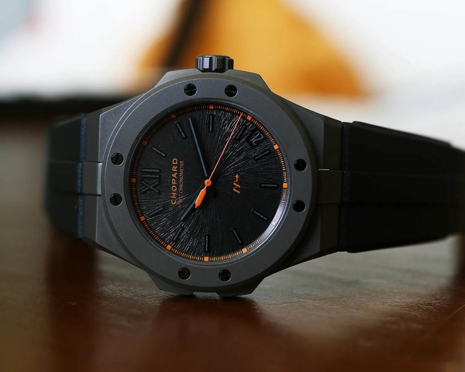 Black Chopard wristwatch with textured dial, orange accents, and black rubber strap on a wooden surface.