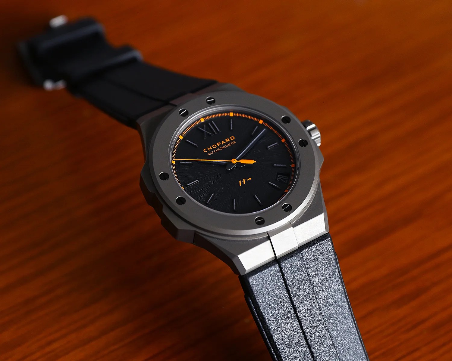 Black dial Chopard wristwatch with orange accents, titanium case, and black rubber strap on a wooden surface.