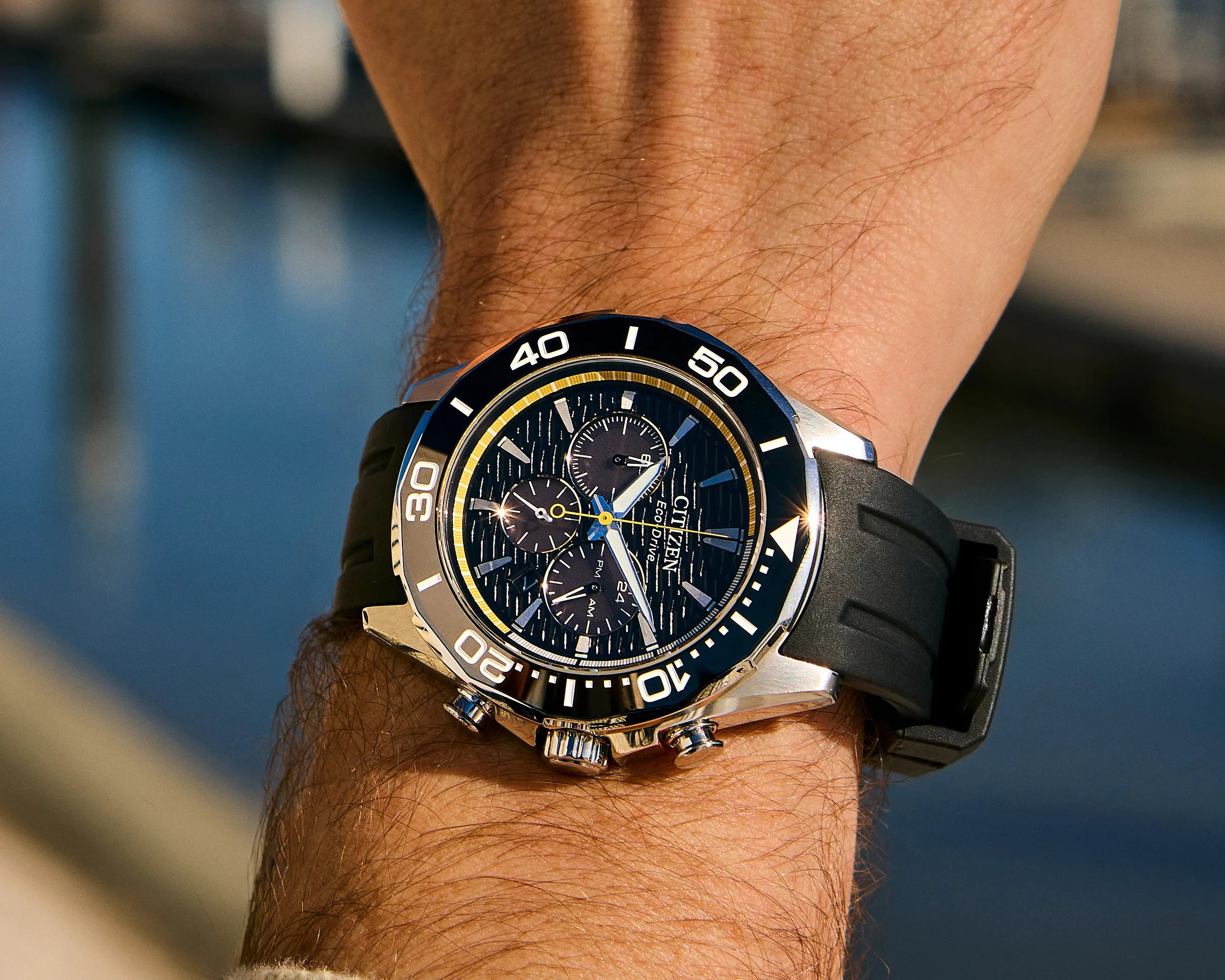 Citizen Eco-Drive chronograph watch with black dial, silver case, and black rubber strap on a wrist.