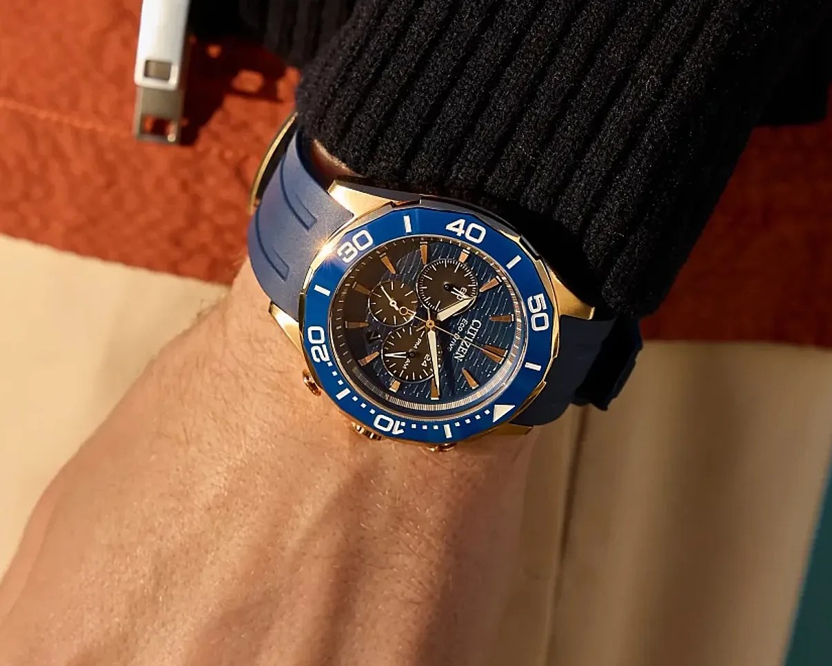 Blue and gold Citizen chronograph watch with blue rubber strap worn on a wrist.