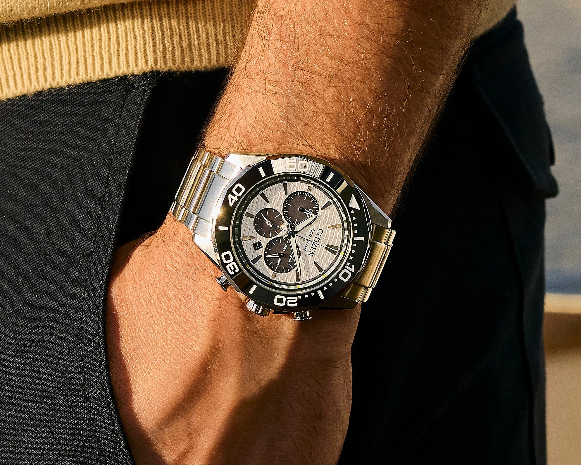 Silver Citizen Eco-Drive chronograph watch with black bezel and white textured dial on a wrist.
