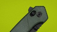 Close-up of a green textured folding knife handle with black screws and a thumb stud on a lime green background.
