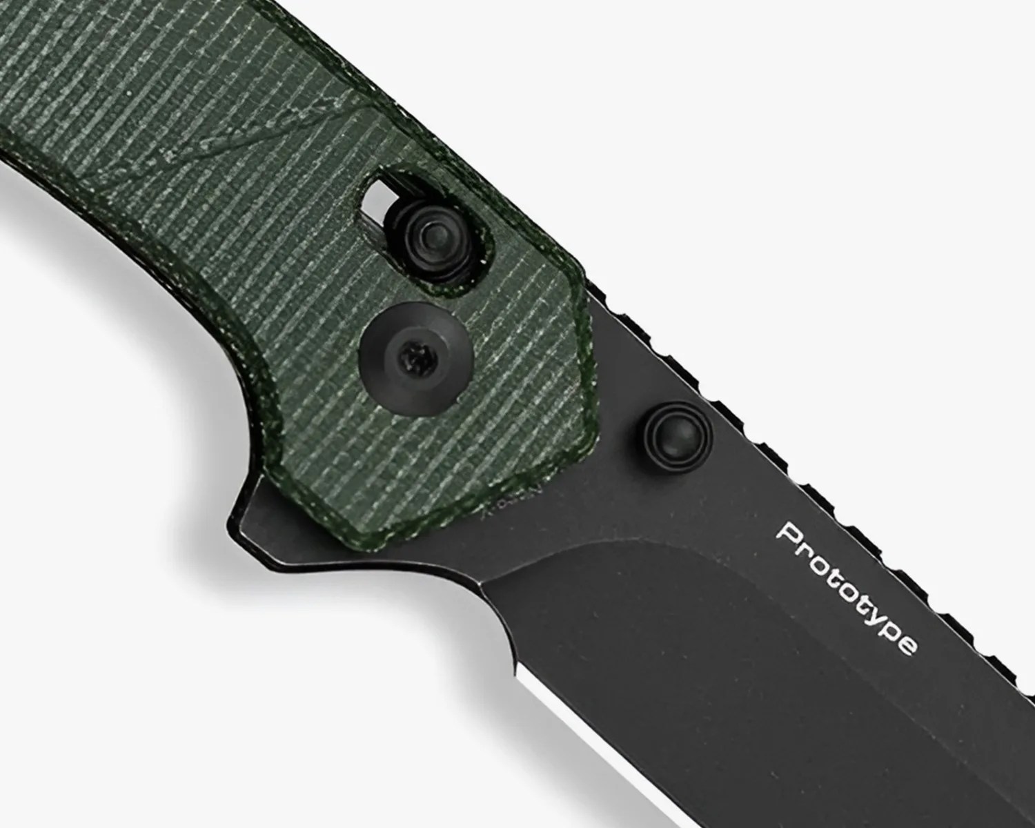 Close-up of a black folding knife blade with "Prototype" text and a textured dark green handle.