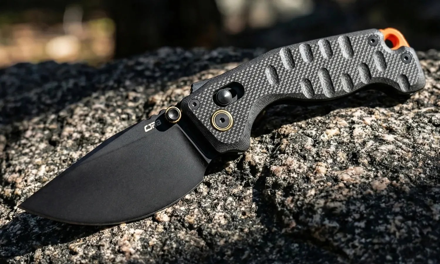 Black folding knife with textured gray handle and orange lanyard hole resting on a granite rock.