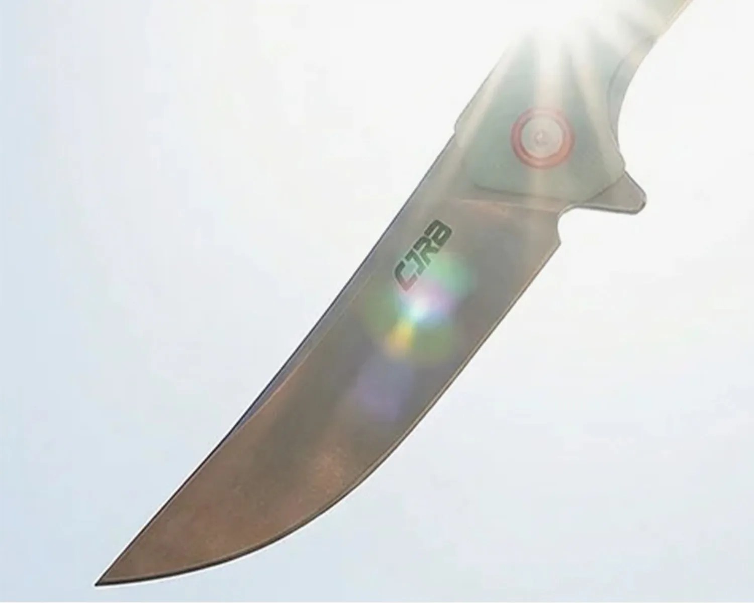 Close-up of a metallic knife blade with "CRB" engraved, illuminated by bright sunlight and lens flare.