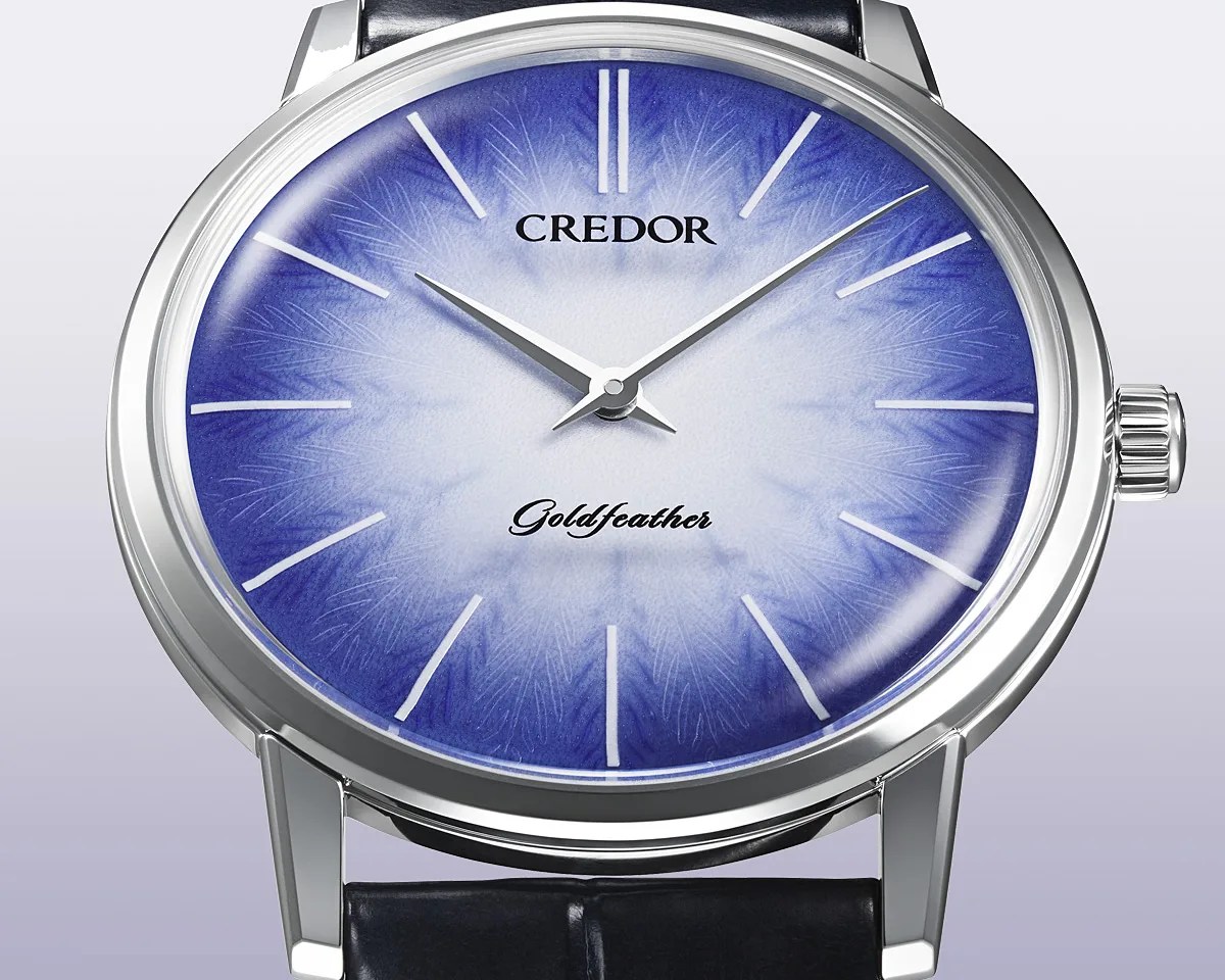 Silver round watch with a blue and white gradient dial featuring feather-like patterns and black leather strap.