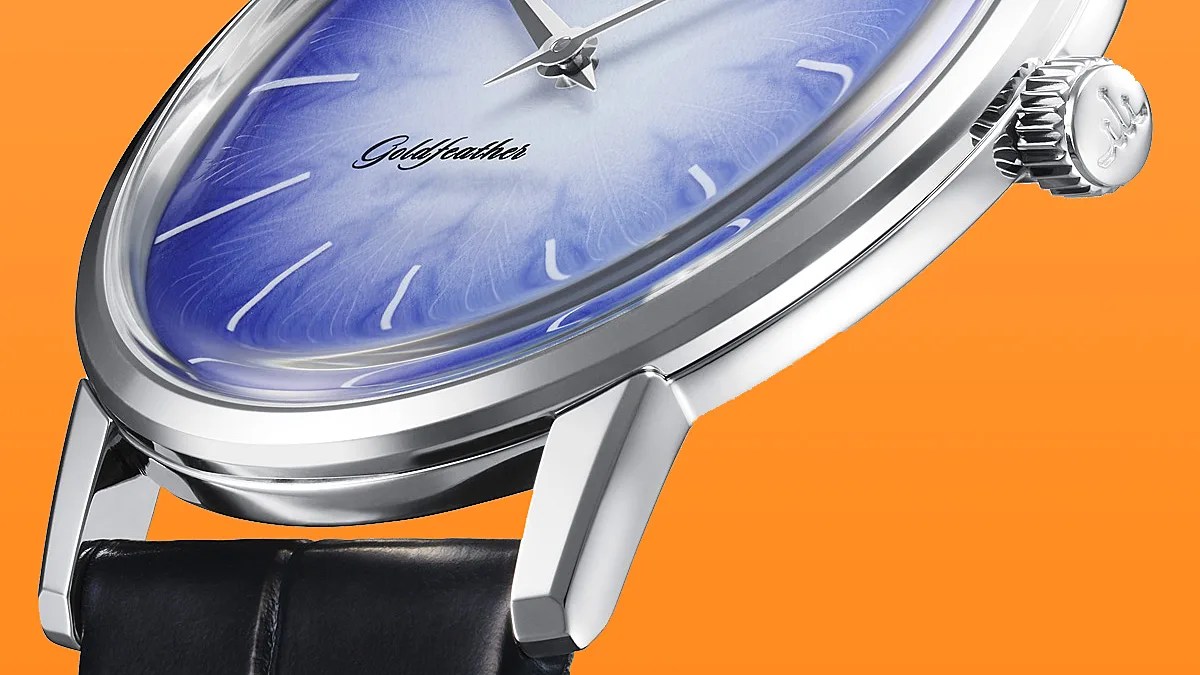 Close-up of a silver watch with a blue textured dial, black leather strap, and "Goldfeather" logo on an orange background.