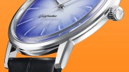 Close-up of a silver watch with a blue textured dial, black leather strap, and "Goldfeather" logo on an orange background.
