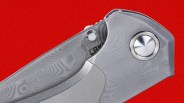 Close-up of a folding knife with a patterned metal handle and a circular pivot screw against a red background.