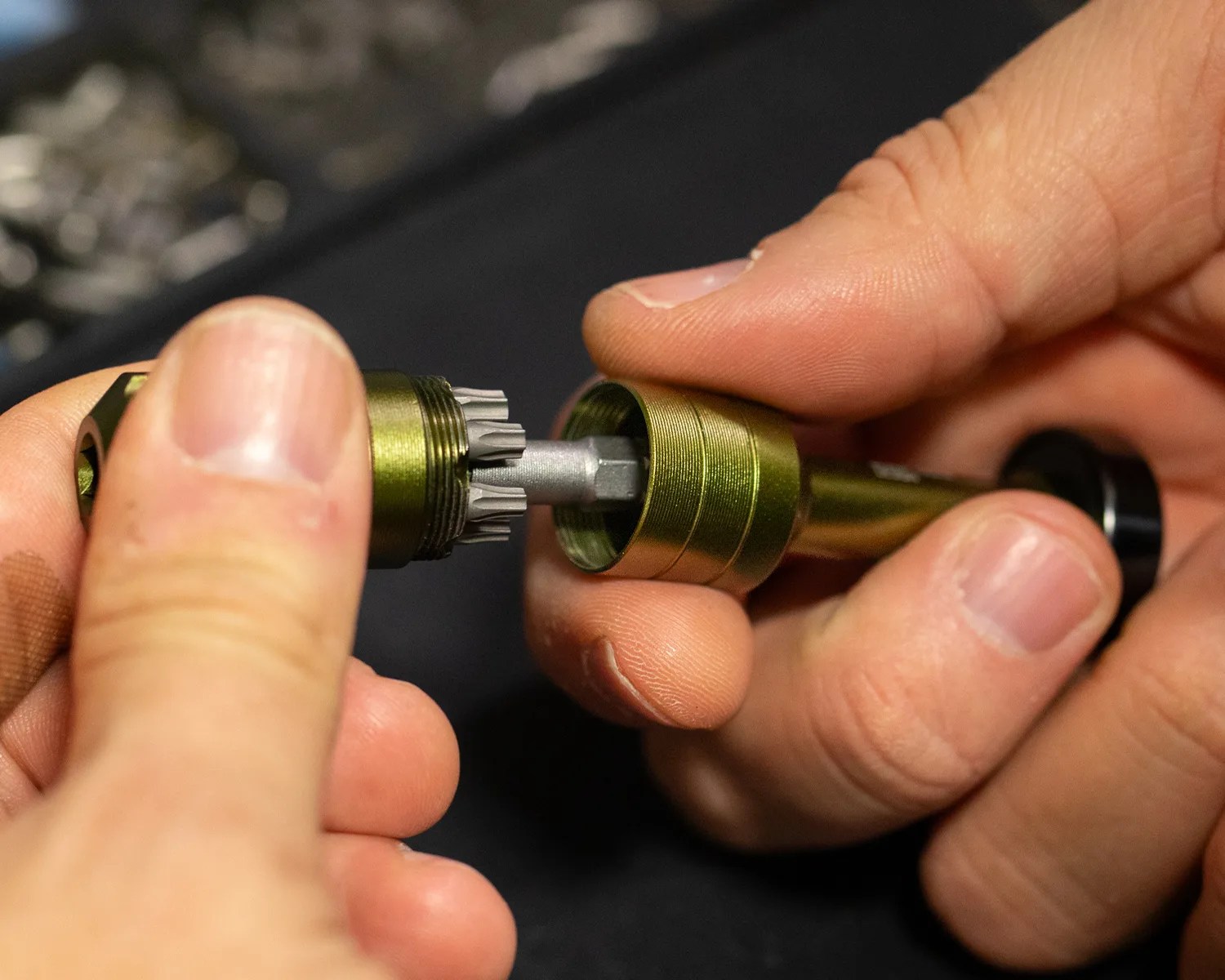Hands holding and assembling a small metallic tool with a greenish-gold finish and a star-shaped bit.