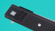 Close-up of a black textured folding knife handle with two silver screws on a turquoise background.