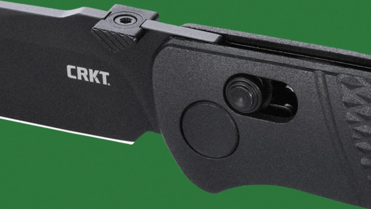 Black folding knife blade with CRKT logo and textured black handle on green background.