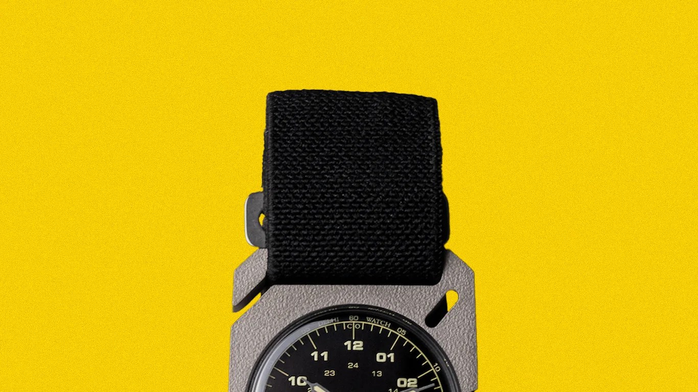 Black fabric strap watch with a round black dial and beige numerals on a yellow background.