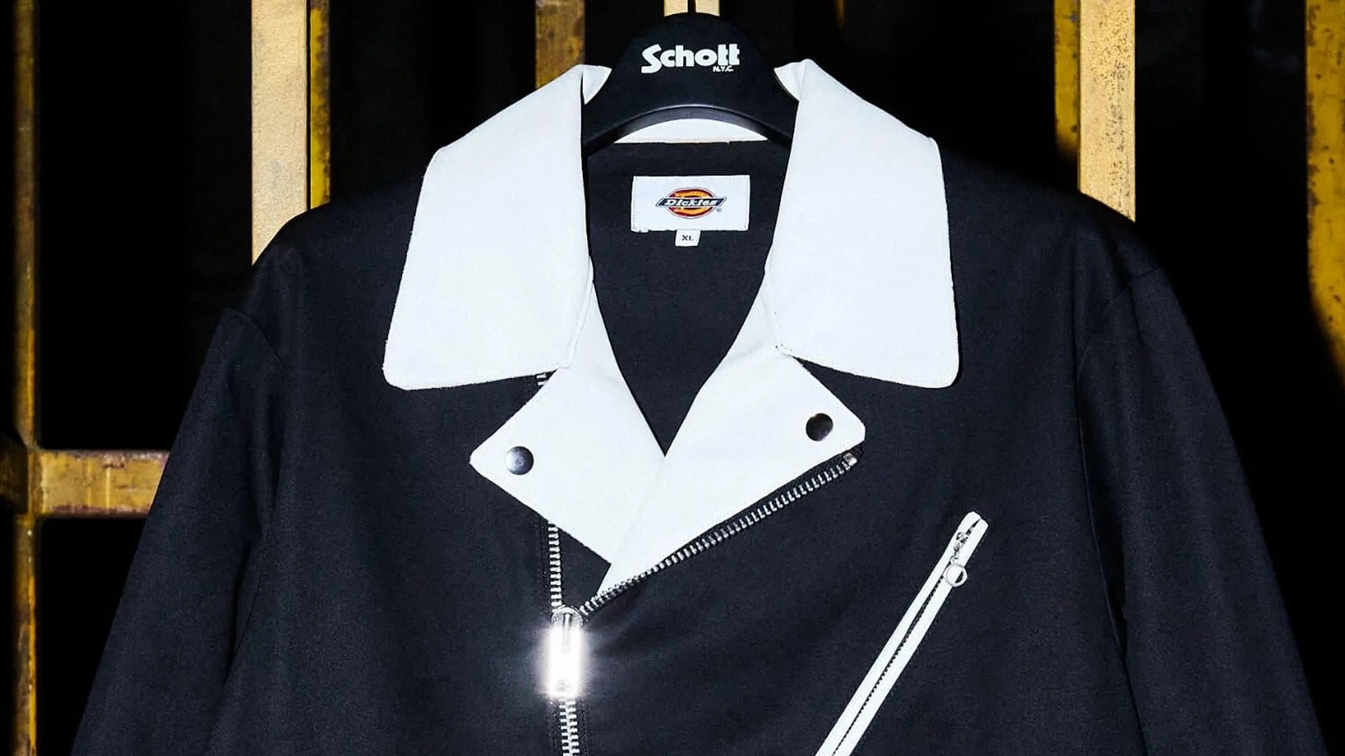 Black jacket with large white collar and white zippered chest pocket hanging on a Schott hanger.