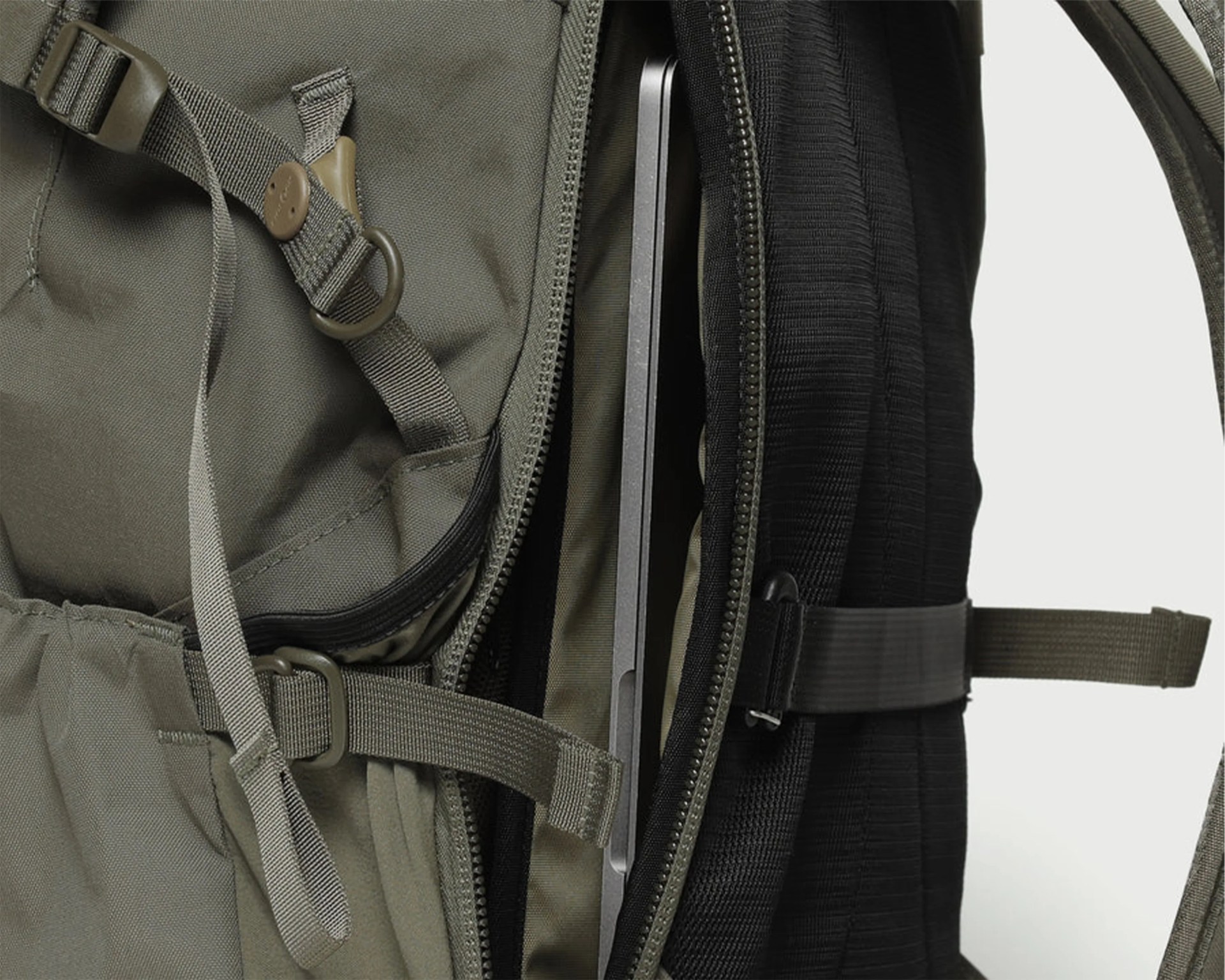 Close-up of an olive-green backpack with a padded black laptop compartment holding a slim laptop.