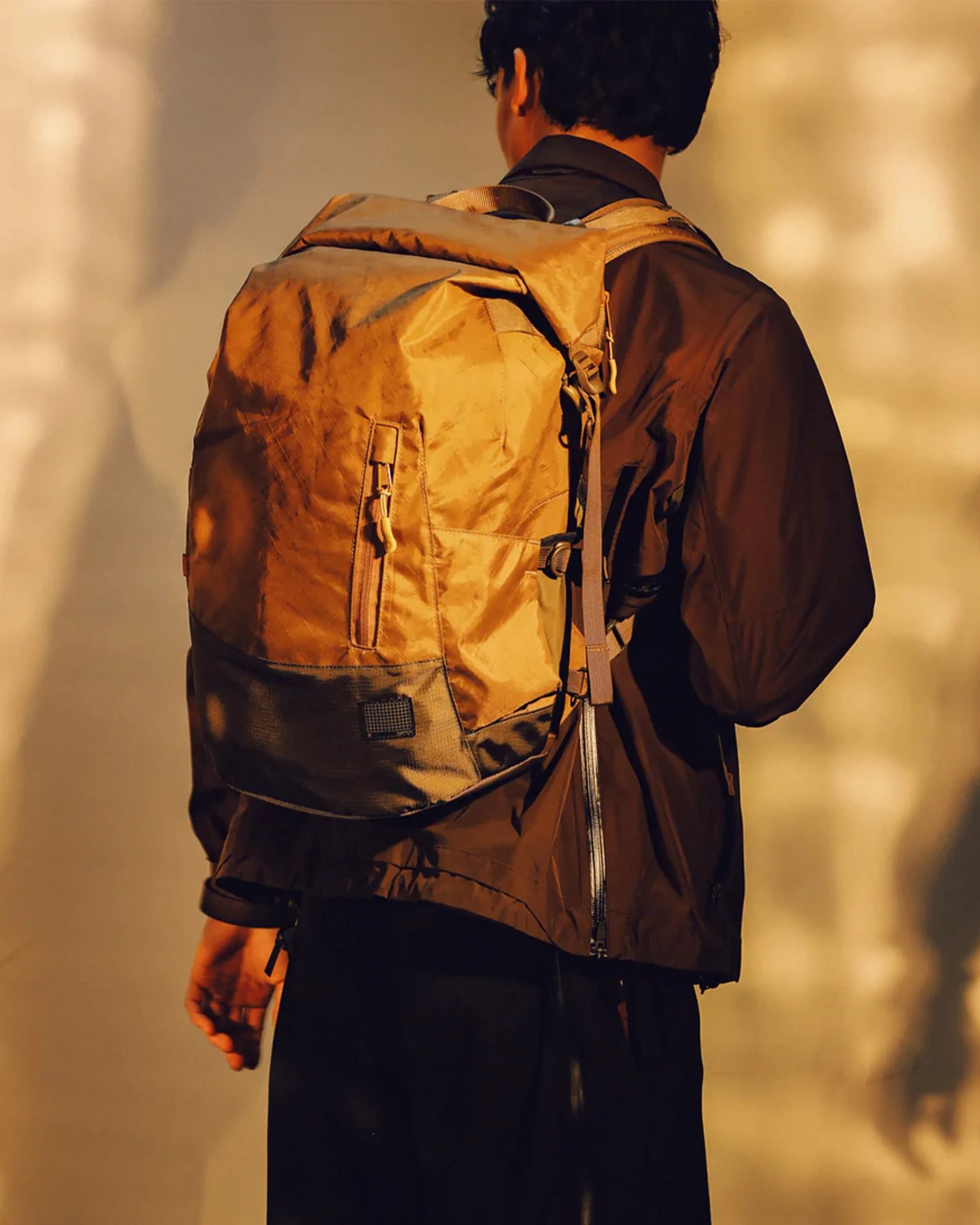 Brown and black roll-top backpack worn by a person in a brown jacket.