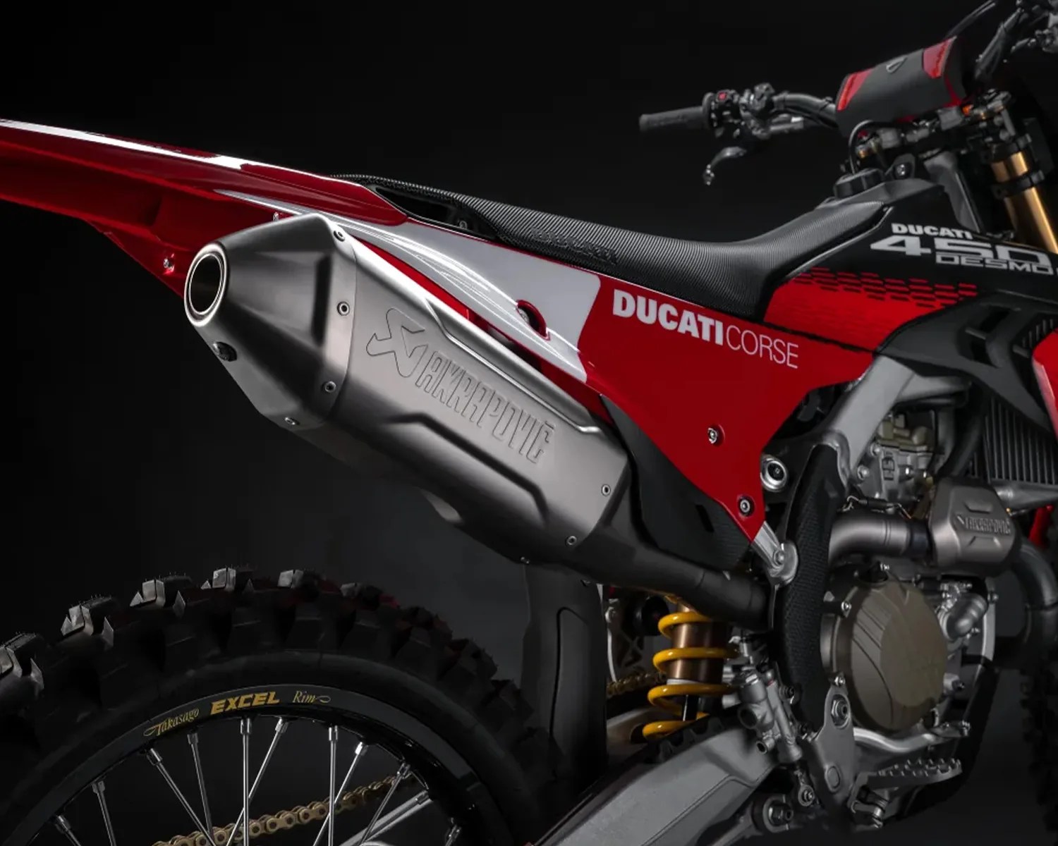 Close-up of a red Ducati Corse dirt bike showing the Akrapovič exhaust, rear tire, and suspension.