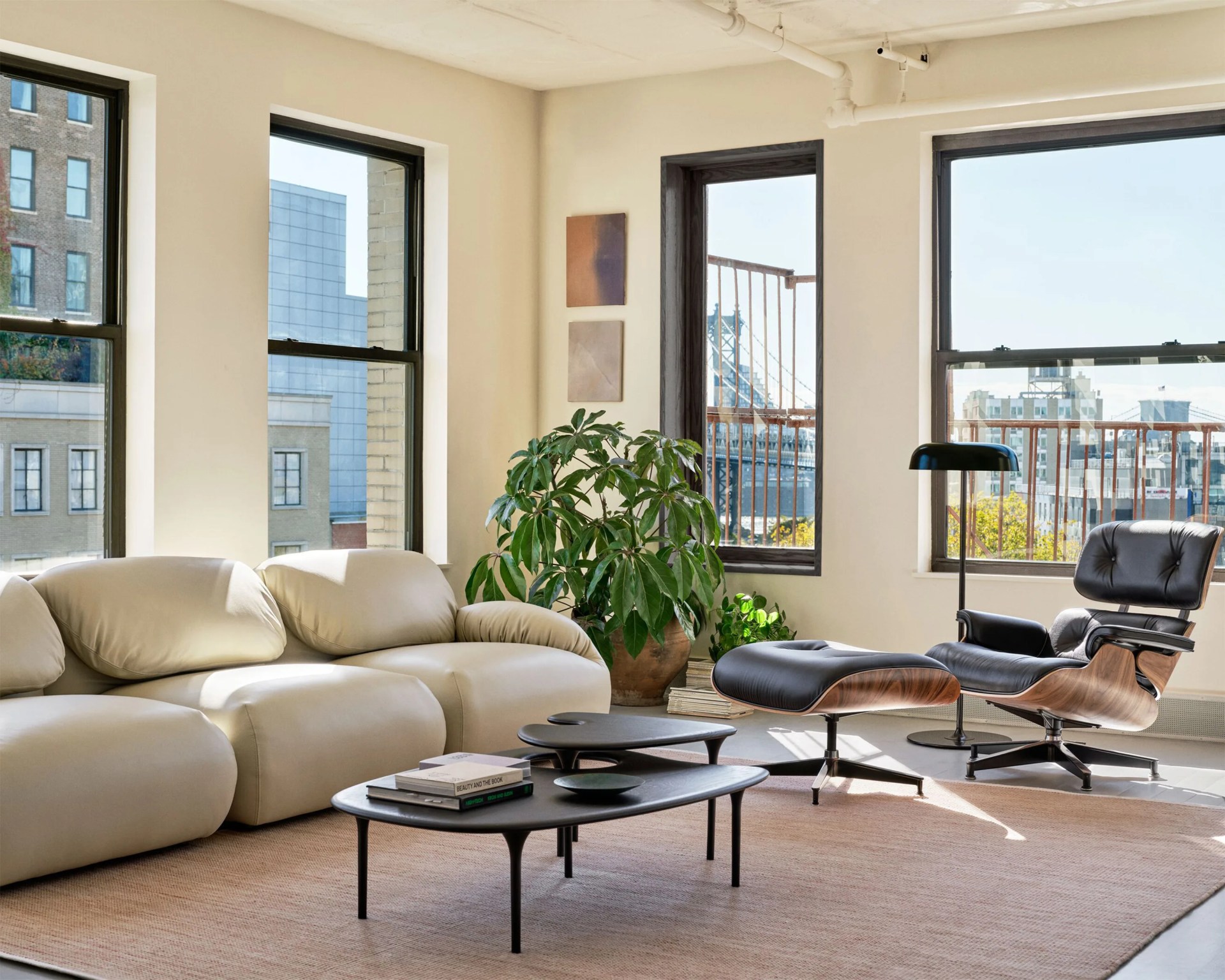 Beige leather sofa, black leather lounge chair with ottoman, black nested coffee tables, and large green plant in a bright living room.