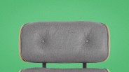 Gray fabric cushioned chair backrest with wooden edges against a green background.
