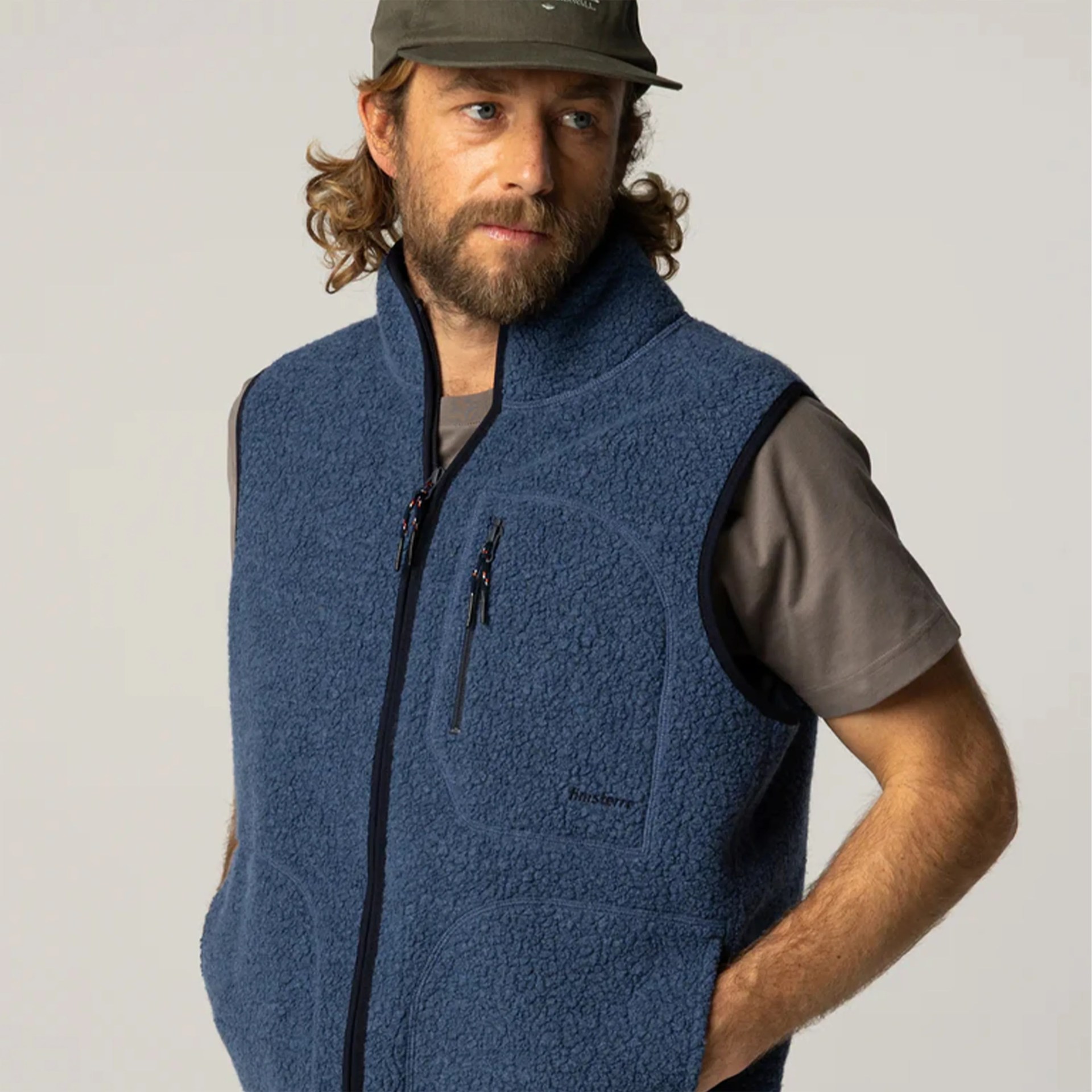 Man wearing a blue zip-up fleece vest over a gray short-sleeve shirt and an olive green cap.
