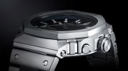 Close-up of a silver metal wristwatch with a black dial and "MR-G" engraved on the crown.