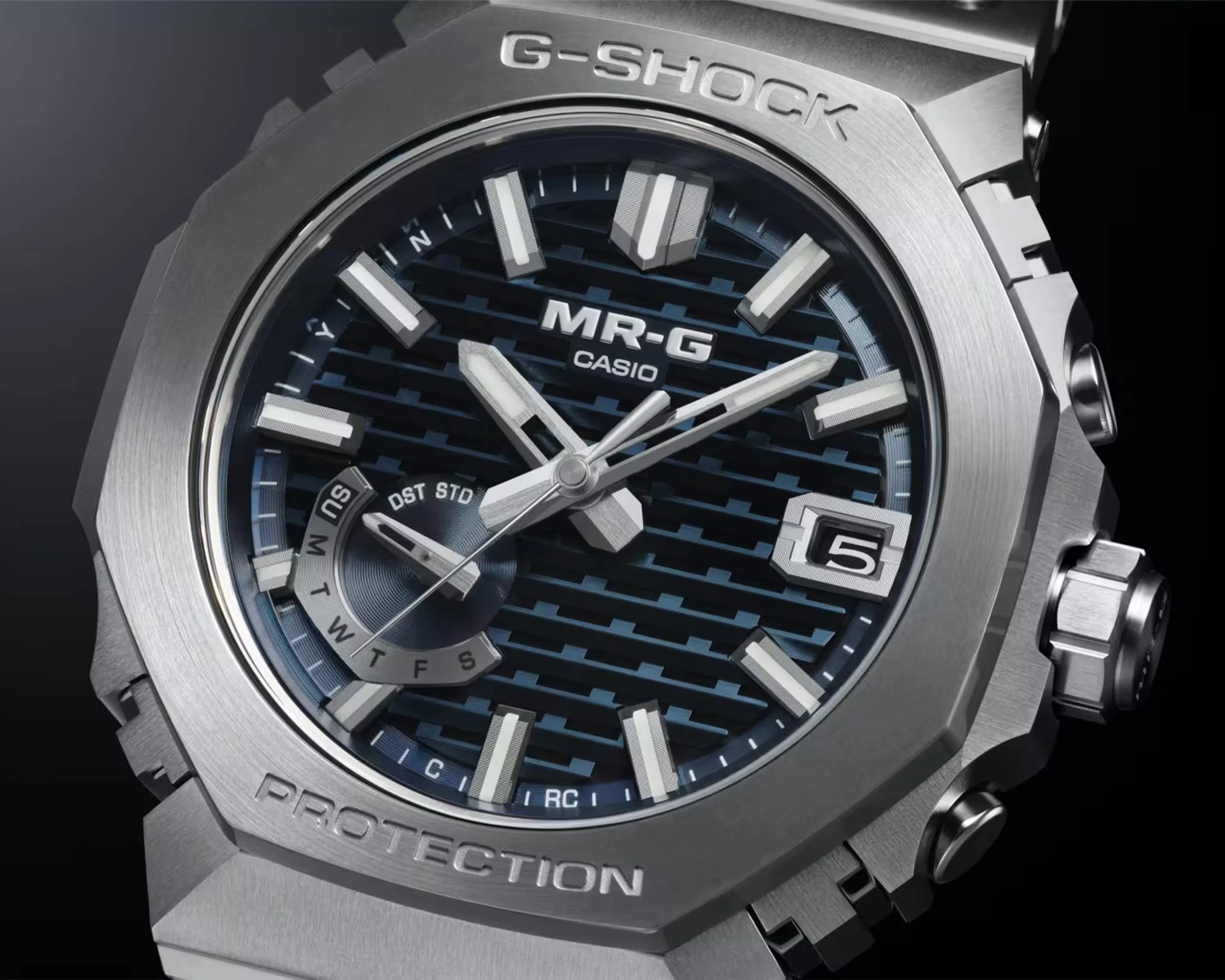 Close-up of a Casio G-Shock MR-G watch with a blue patterned dial, silver hour markers, and date display.