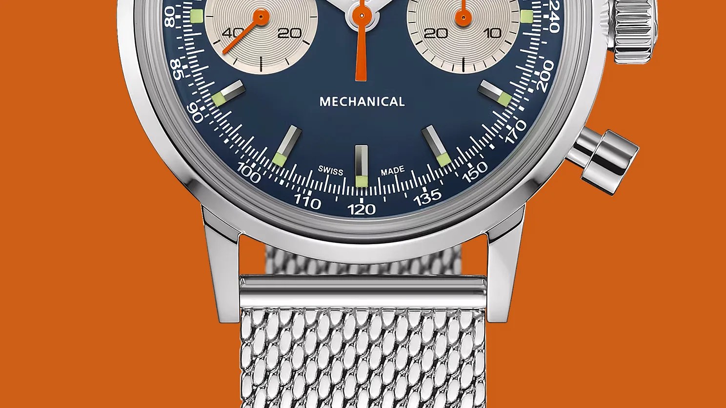 Close-up of a blue dial mechanical watch with silver mesh strap and orange chronograph hands on an orange background.