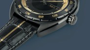 Close-up of a black wristwatch with gold accents, a black bezel with gold numerals, and a black leather strap with a gold stripe.