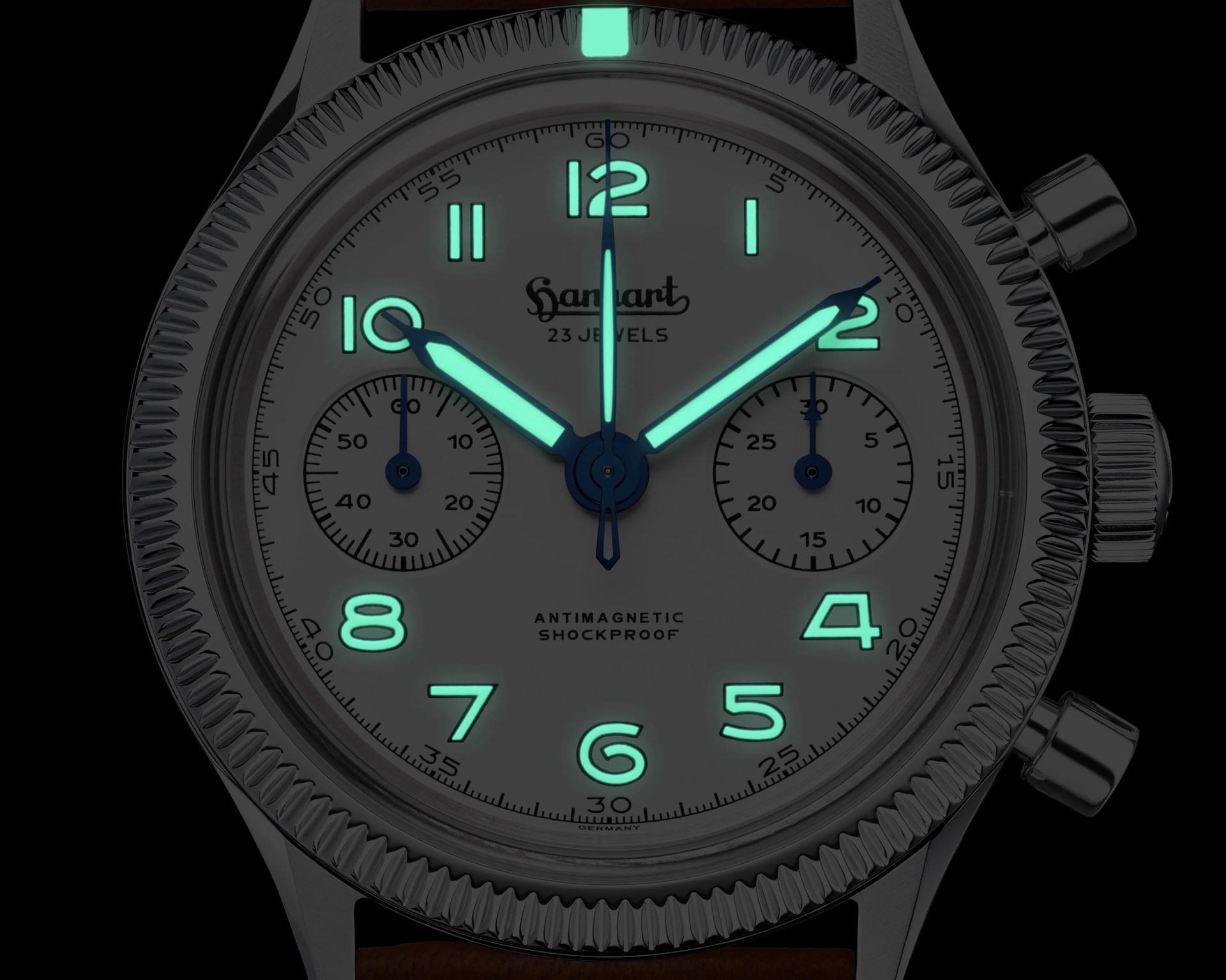 Close-up of a Hanhart chronograph watch face with luminescent hands and numerals glowing green in the dark.