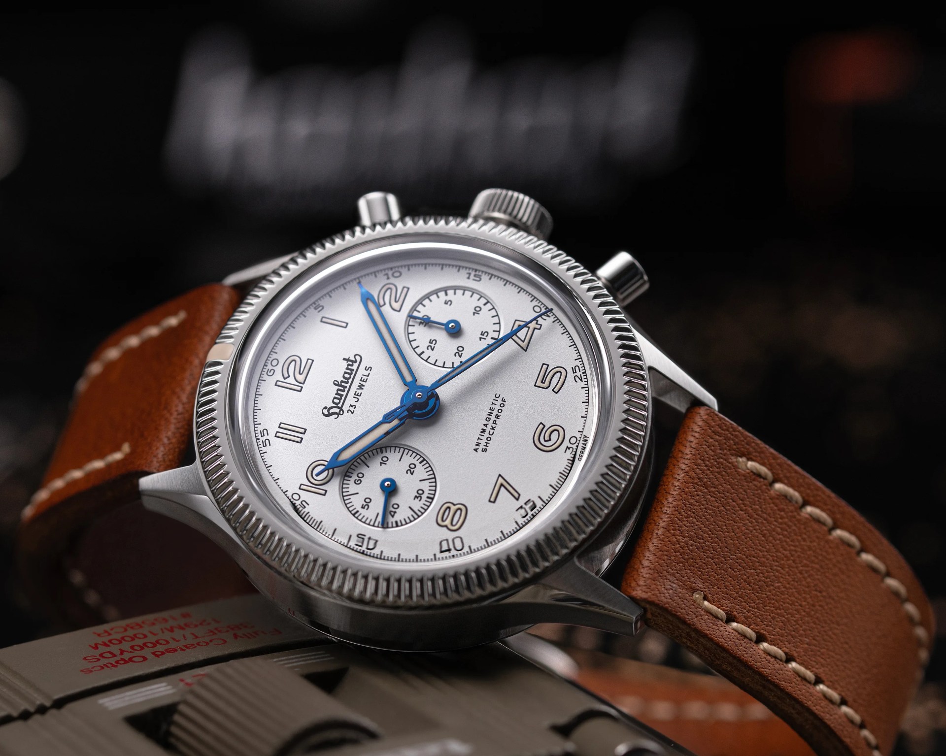 Stainless steel wristwatch with white dial, blue hands, and brown leather strap with white stitching.