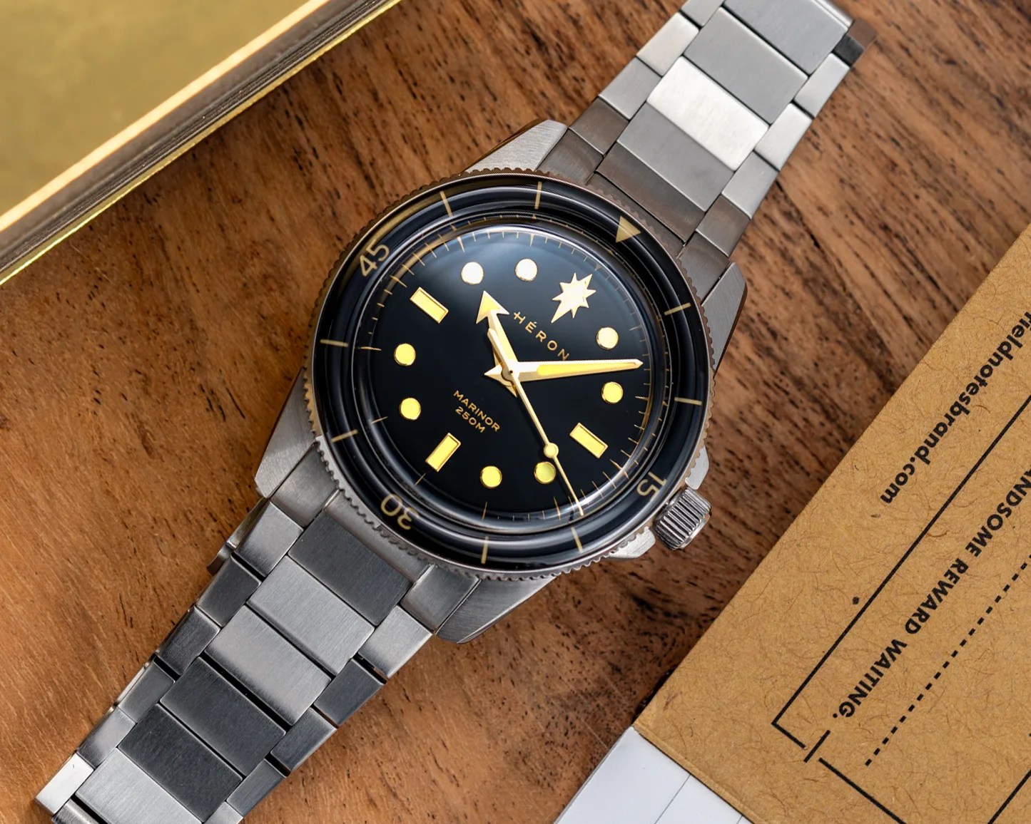Stainless steel wristwatch with black dial, gold markers, and rotating bezel on a wooden surface.